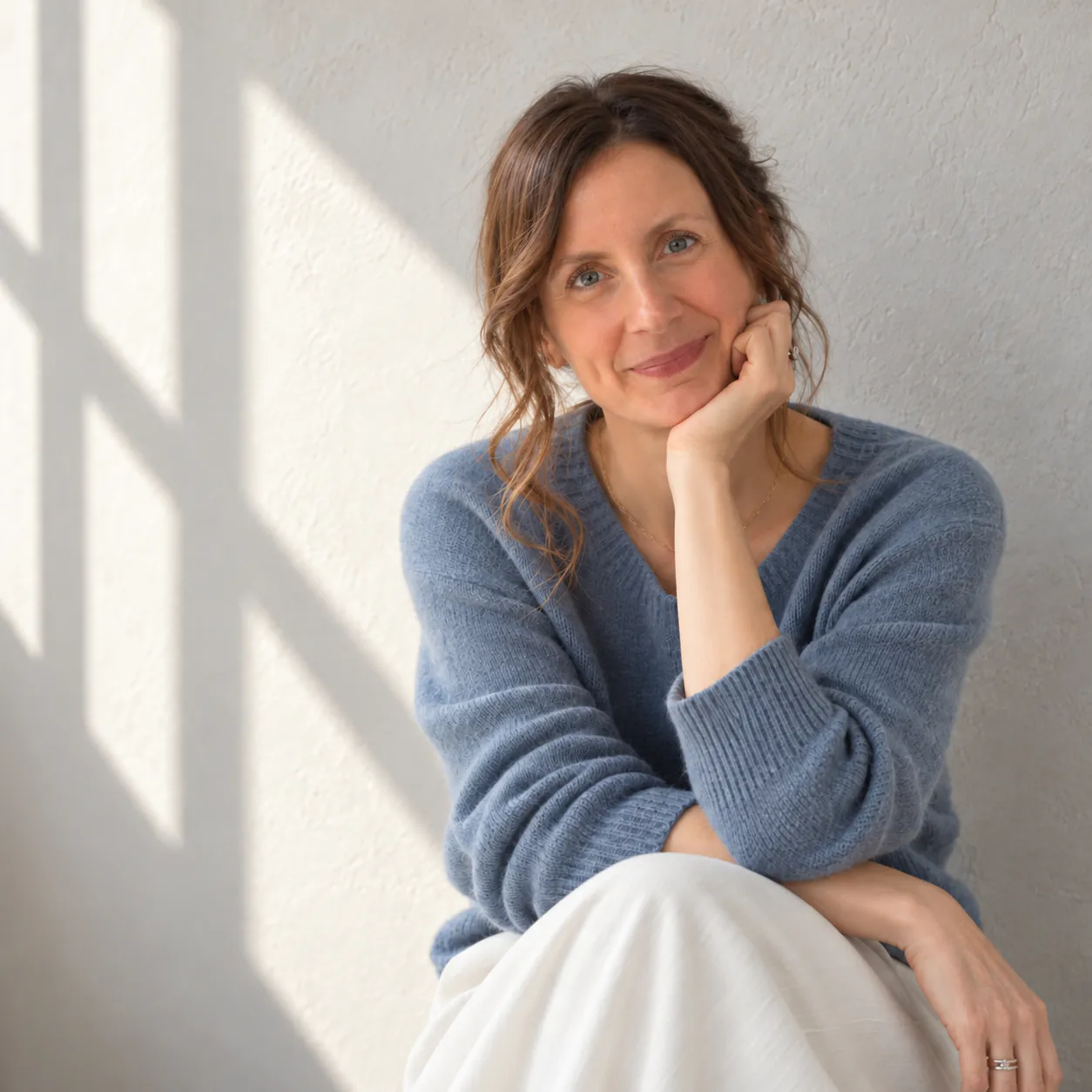 Martina Bartolomucci, life coach, smiling, chin resting on one hand, in soft window light